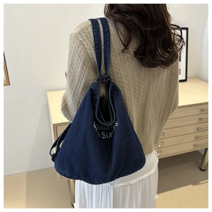 Detail of dark blue denim tote bag with embroidered white lettering shown on shoulder