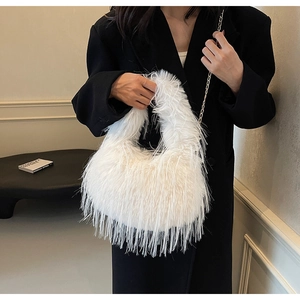 Nahaufnahme der weißen Plüschtasche mit Goldkette vor einem schwarzen Blazer