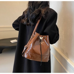 Detail view of brown glossy bucket bag with white butterfly charm on a black coat