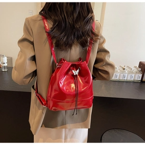 Detail of red glossy PU leather bucket backpack with silver butterfly charm and drawstring