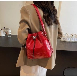 Detail of red glossy patent leather bucket bag with metal butterfly buckle and drawstring