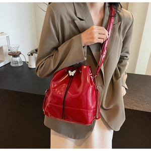 Detail of bright red drawstring bucket bag with butterfly metal buckle and slim strap