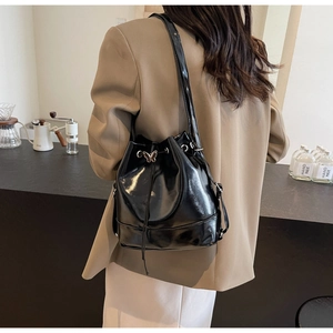 Detail of black patent leather bucket bag with silver butterfly charm worn by a model
