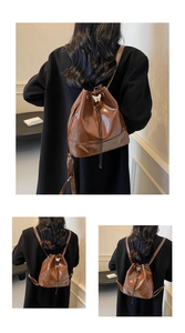 Detail of glossy brown drawstring bucket bag featuring a silver butterfly charm pendant