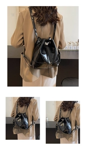 Detail of black glossy leather backpack featuring silver butterfly hardware and drawstring