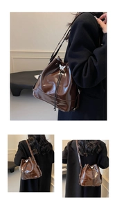 Detail view of dark brown patent leather bucket bag with silver butterfly drawstring toggle