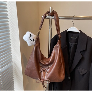 Detail of brown leather tote featuring lace-up design and a plush panda charm on the strap