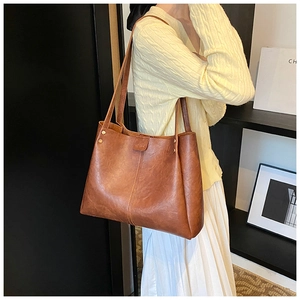 Brown vintage faux leather tote bag with gold rivets shown in a stylish shoulder carry pose