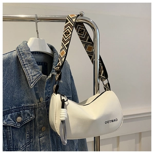 Close-up of white crescent crossbody bag with geometric wide strap and knotted tassel