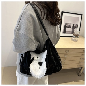 Détail d'un cabas noir brillant avec un patch chiot en peluche blanche porté à l'épaule