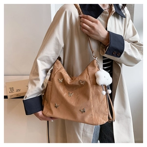 Detail of camel nylon hobo bag with butterfly studs and cloud charm worn on a trench coat
