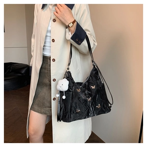 Detail of black tote bag with gold butterfly accents and plush cloud charm on a trench coat