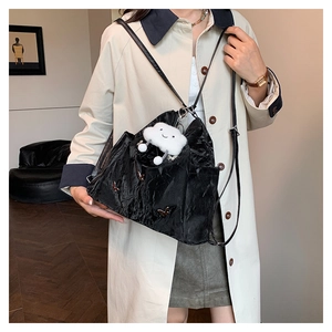 Detail of black pleated tote bag with silver butterfly charm and white cloud plush toy