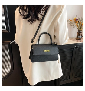 Detail of black pebbled leather crossbody bag with yellow Fashion text on model