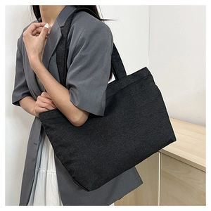Minimalist black canvas tote bag shown as a shoulder bag on a model in a grey blazer