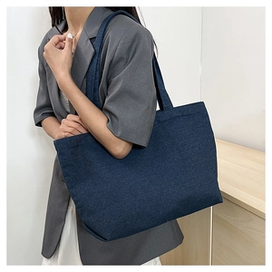 Detail of a large navy canvas tote bag worn by a model in a minimalist indoor setting