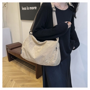 Detail of beige nylon crossbody bag featuring a wide adjustable strap and metal logo