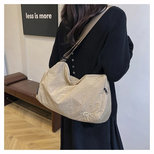 Detail of a large beige nylon pleated crossbody bag with black adjustable strap on model