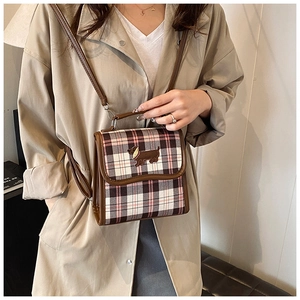 Detail of plaid crossbody bag with embroidered dog patch and brown leather trim