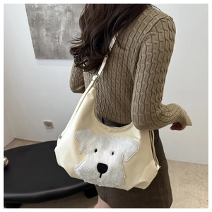 Détail du sac fourre-tout crème avec écusson chiot en peluche porté à l'épaule