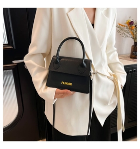 Detail of black pebbled leather crossbody bag with yellow Fashion text on white blazer