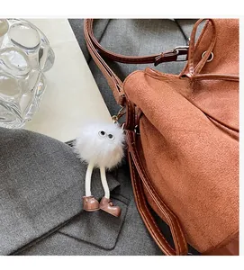 Detail of brown suede bucket bag with drawstring closure and cute white plush charm