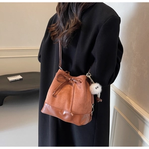 Detail of drawstring bucket bag featuring brown suede texture and plush ball charm