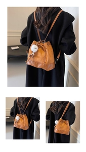 Detail of brown suede bucket bag with drawstring closure and white plush charm accessory