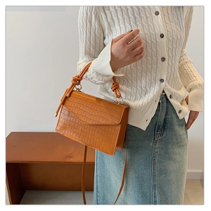 Detail of orange brown crocodile embossed crossbody bag with creative knot handle