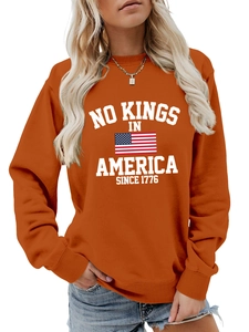 Detail of orange crewneck sweatshirt featuring white NO KINGS IN AMERICA 1776 graphic