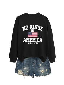 Detail of a black sweatshirt with 'No Kings In America' slogan and ripped denim shorts