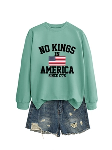 Detail of mint green crewneck sweatshirt with No Kings print and ripped denim shorts