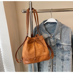 Close-up of brown suede bucket bag with drawstring bow detail hanging on metal rack