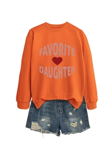 Flat lay of an orange crewneck sweatshirt with 'FAVORITE DAUGHTER' text and denim shorts