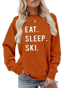 Close-up of burnt orange sweatshirt featuring white Eat Sleep Ski bold graphic print