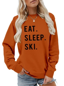Close-up of burnt orange crewneck sweatshirt featuring black EAT SLEEP SKI letter print