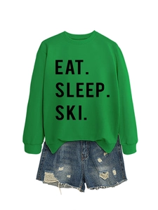 Flat lay of green 'EAT SLEEP SKI' sweatshirt paired with distressed blue denim shorts