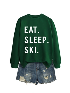Close-up of Eat Sleep Ski white typography on dark green crewneck sweatshirt and denim shorts