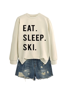 Flat lay of cream crewneck sweatshirt with black Eat Sleep Ski text and denim shorts