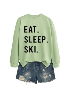 Flat lay of light green crew neck sweatshirt with EAT SLEEP SKI text and ripped denim shorts
