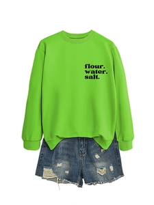 Dettaglio della felpa verde acceso con scritta stampata e pantaloncini in denim strappati