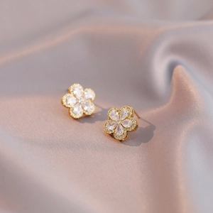 Elegante Blumenohrringe aus Gold mit Zirkonia auf champagnerfarbenem Seidenhintergrund
