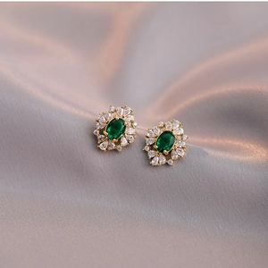 Elegant gold earrings with emerald green zircon and white crystals on grey silk fabric