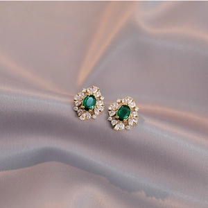Elegant emerald green oval earrings with zircon halo on champagne silk background
