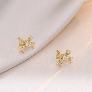 Élégantes boucles d'oreilles nœud dorées avec zircons étincelants sur tissu satiné luxe