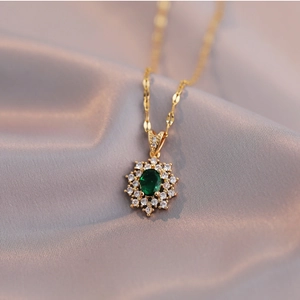Gold necklace with sunburst pendant featuring an emerald green oval stone and zircon accents