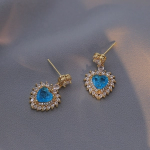 Detail of heart-shaped earrings with blue zircon center and gold-tone finish