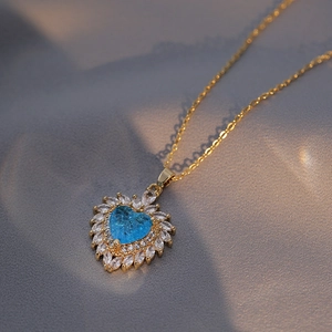 Golden heart necklace with a blue sapphire-like stone surrounded by crystals on silk