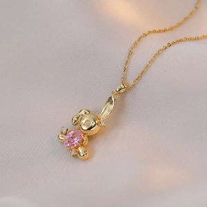 Golden rabbit pendant necklace with pink zircon gemstone on a warm textured background