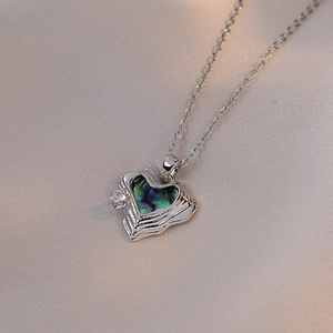 Elegant heart pendant necklace with iridescent shell inlay and zircon on silk background